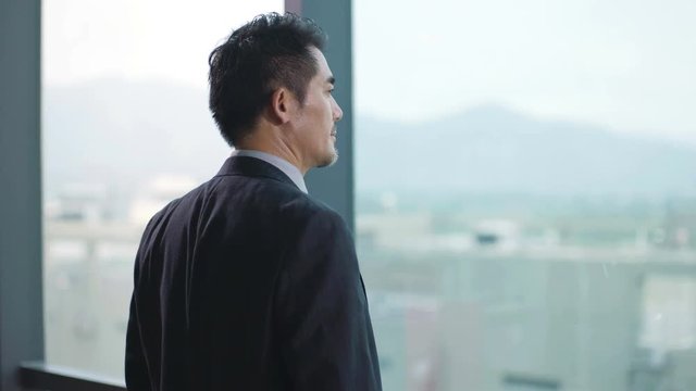 asian corporate executive standing in front of window thinking in office