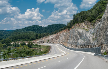 Appalachian Mountain Highway:  A four lane divided highway curves between a winding river and a steep cut rock face in eastern Tennessee.