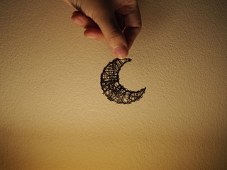 Basketry wiring crescent moon, held by hand, dark yellow spotlight cement wall background