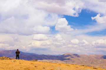 Mountain landscape. Single man stands on the edge above the dry Tibetan plateau, highlands of Tibet, China.
