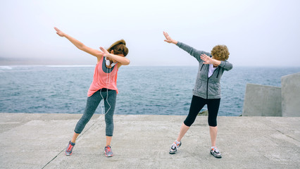 Senior and young woman making dab dance outdoors by sea pier