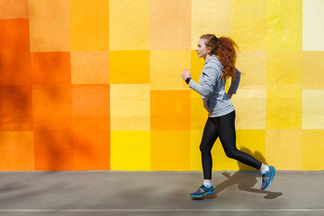 Fototapeta na wymiar Side view of woman running against bright wall