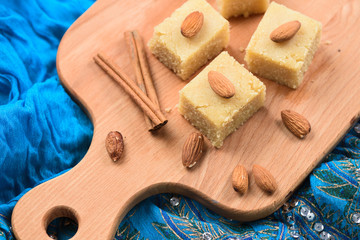 Halava, Indian sweetmeats cut in squares decorated with almonds on wooden board on indigo cloth