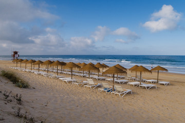 Fototapeta na wymiar Straw umbrellas on the beach of Barrosa de Sancti Petri, Chiclana, Cadiz, Spain