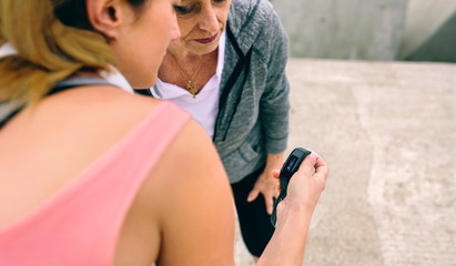 Senior woman looking smart watch with female coach outdoors