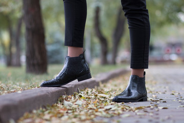 Python leather shoes. A girl steps in boots on an autumn foliage in a park