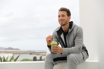 Healthy man drinking green smoothie at home terrace. Sport athlete with spinach cold pressed juice...