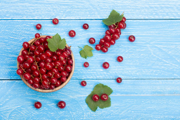 Red currant berries in a wooden bowl with leaf on the blue wooden background with copy space for your text. Top view