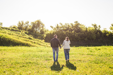 Man and woman holding hands and walking on nature, back view