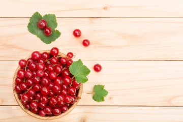 Red currant berries in a wooden bowl with leaf on the light wooden background with copy space for your text. Top view