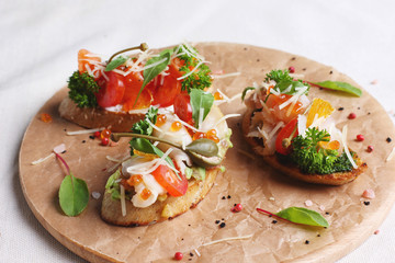 Sandwiches with red fish, tomato, mozzarella and herbs on wooden round board