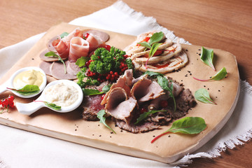 Cold smoked meat plate with greens and mustard on wooden board