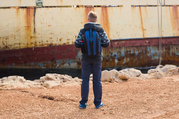 Obraz na płótnie Canvas Male tourist looking at an abandoned ship on the sea or ocean back view. Adventure and tourism concept