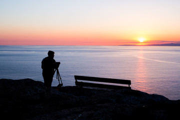 Fototapeta premium man photographer taking photos of sunset at the sea