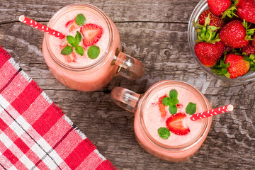 Glass of strawberry yogurt or smoothie with mint leaves on old wooden background. Top view