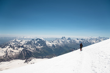 Obraz premium Mountaineer in the mountains strolls along the snow slope against the background of snow-capped peaks