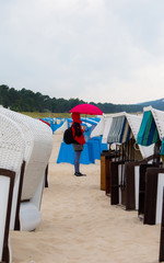 A woman stands in bad weather with an umbrella between beach chairs on the beach