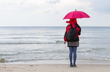 A woman stands with an umbrella and a bottle mail on the beach