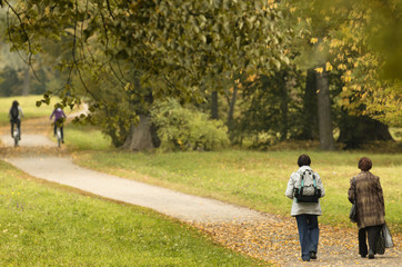Obraz premium Two old ladies and two cyclists in the distance on autumn path - Unidentified people with their backs to the beholder