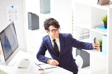Young employee with smartphone making his selfie by workplace