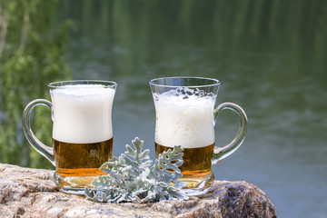 Two of beer mug are stand on a rock above the river