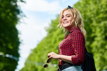 Cheerful blonde girl with sunglasses looking at camera while relaxing in amusement park