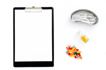 Doctor's workplace in clinic. Clip pad, colored pills and cuvette with ampoulie on white background top view mockup