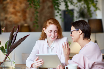 Pretty young white collar worker sharing ideas with her experienced colleague while having informal working meeting at cozy restaurant