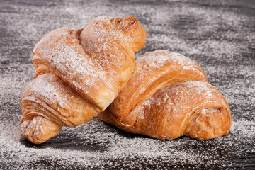 two croissant sprinkled with powdered sugar on black stone background closeup