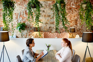 Profile view of female HR manager conducting interview with young red-haired applicant for position...