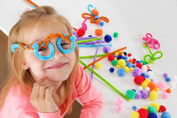 fillette 6 ans jouant avec des pompons de couleurs et des fils chenille - obrazy, fototapety, plakaty