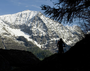Landscape: backlight of man on the trail leading to Alp Vova, Salecchio, Casa Francoli with an electric bicycle E-bike, snowy mountains background of Fromazza Valley, Piedmont, Ossola, Alps, Italy