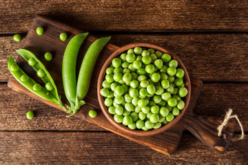 Fresh green peas in ceramic bowl on dark wooden background