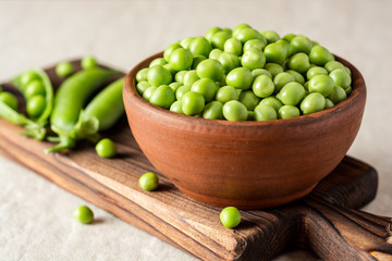 Fresh green peas in ceramic bowl on gray stone background