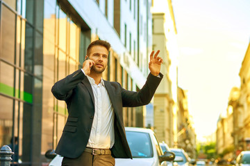 Young businessman talking on a phone and waving for a taxi