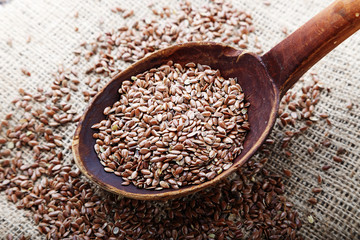 The seeds of flax are scattered on the table, on a linen napkin. Seeds in a wooden spoon. Horizontal photo.