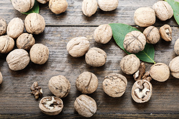 Whole walnuts in the shell are scattered on a wooden background, with walnut leaves