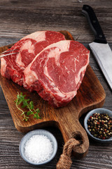 Raw fresh meat Ribeye Steak, seasoning and meat fork on dark bac