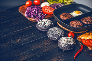 Ingredients for a black burger on a wooden surface