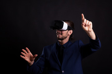 Businessman with a VR headset on head in studio photo on black background. Virtual reality and gestures