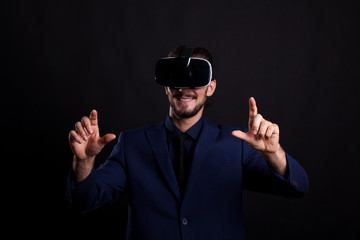 Businessman with a VR headset on head in studio photo on black background. Virtual reality and gestures