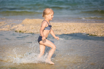 Little cute blonde girl running along the beach
