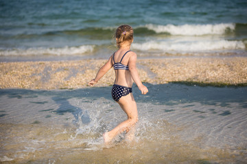 Little cute blonde girl running along the beach