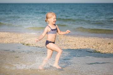 Fototapeta na wymiar Little cute blonde girl running along the beach