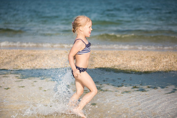 Little cute blonde girl running along the beach