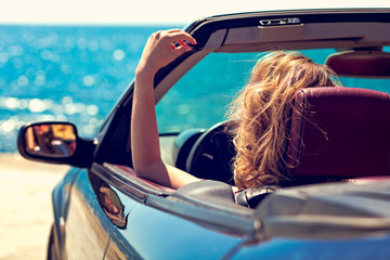 Beautiful blond smiling young woman in convertible top automobile looking sideways while parked...