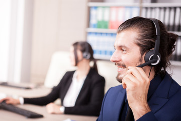 Portrait of man from customer support line in the office and his colleague blurred on the background. Help desk and support