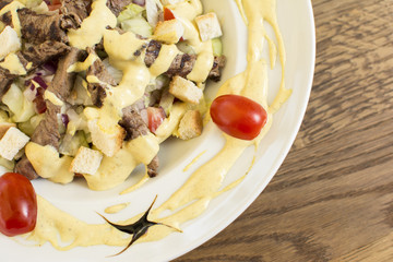 Healthy grilled red meat salad with cheese and croutons. Bacon and lettuce slices in a white plate on a wooden table.