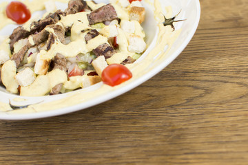 Healthy grilled red meat salad with cheese and croutons. Bacon and lettuce slices in a white plate on a wooden table.