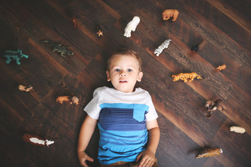 Little boy lying down surrounded by animal toys